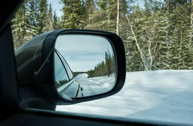 Bilens sidospeglar reflekterar den snöiga vägen.