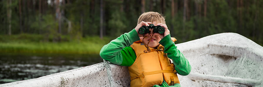 En pojke sitter i en båt och använder kikare