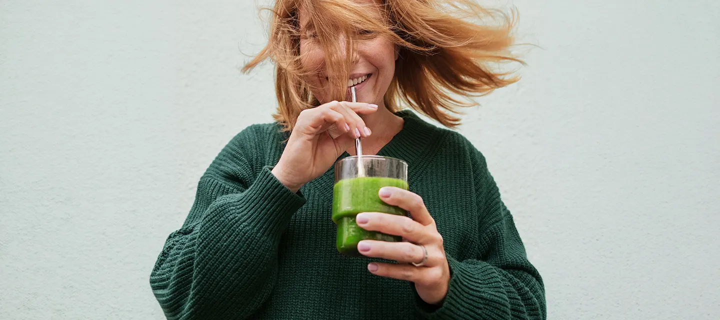 Nainen hymyilee ja juo smoothieta.