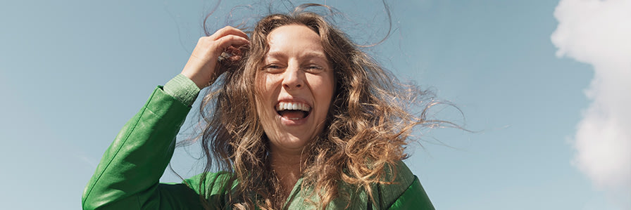 Nainen nauraa ja hiukset hulmuaa tuulessa