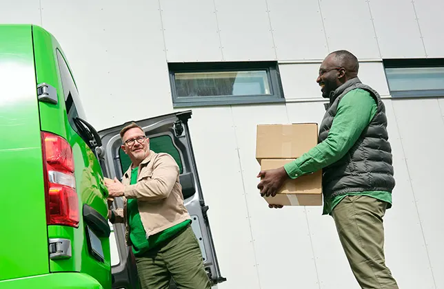 Miehet kantavat laatikoita pakettiautoon.