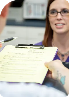 Patient or client filling out medical forms on a yellow clipboard during check-in at a clinic or veterinary office.