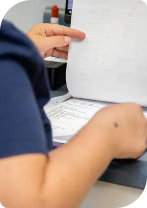 Hands of a vet technician or nurse sorting through a stack of paperwork and forms in a clinical office setting.