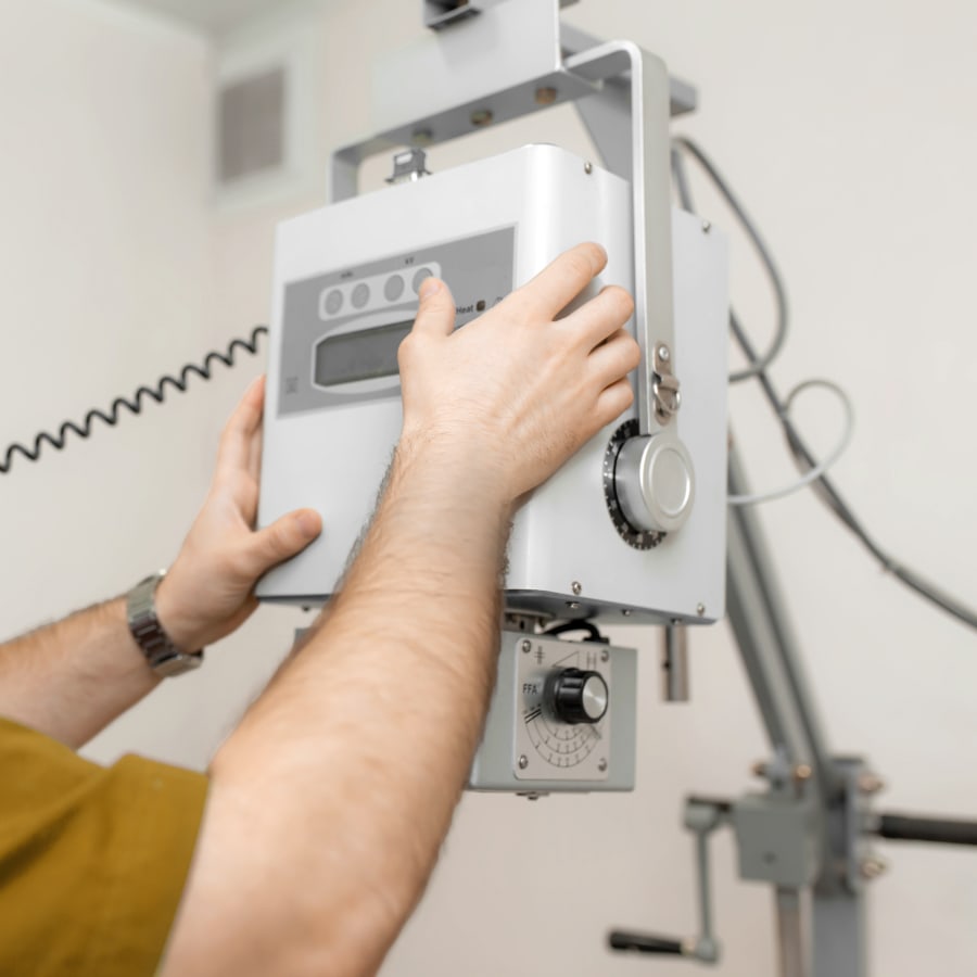 Veterinary technician adjusting a portable digital X-ray machine to capture diagnostic imaging in a clinical setting. Veterinary technician adjusting a portable digital X-ray machine to capture diagnostic imaging in a clinical setting.