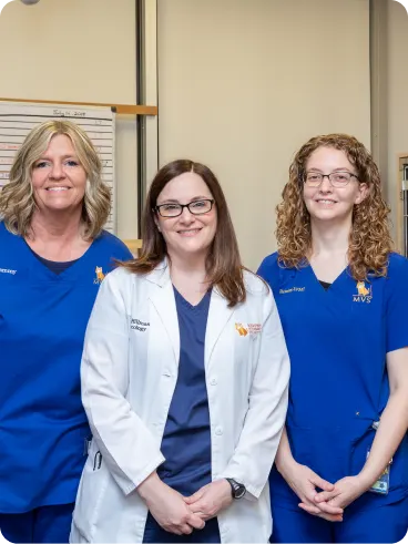 A group portrait of three female veterinary professionals, one wearing a white lab coat and two wearing blue scrubs.