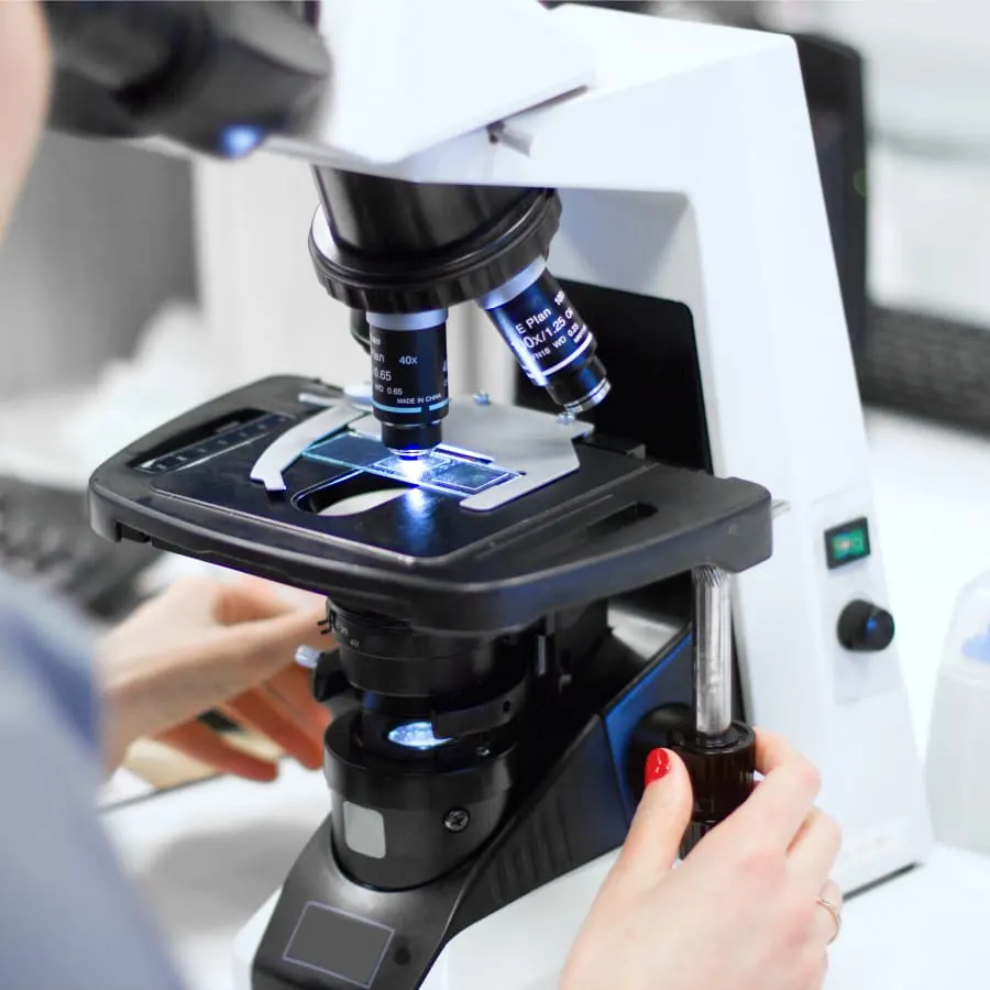 Close-up of a laboratory professional using a binocular compound microscope to analyze a glass slide for diagnostic testing.
