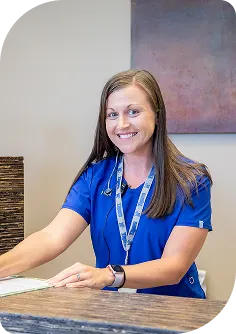 Smiling veterinary receptionist or clinic administrator in a bright blue uniform standing at the front desk.