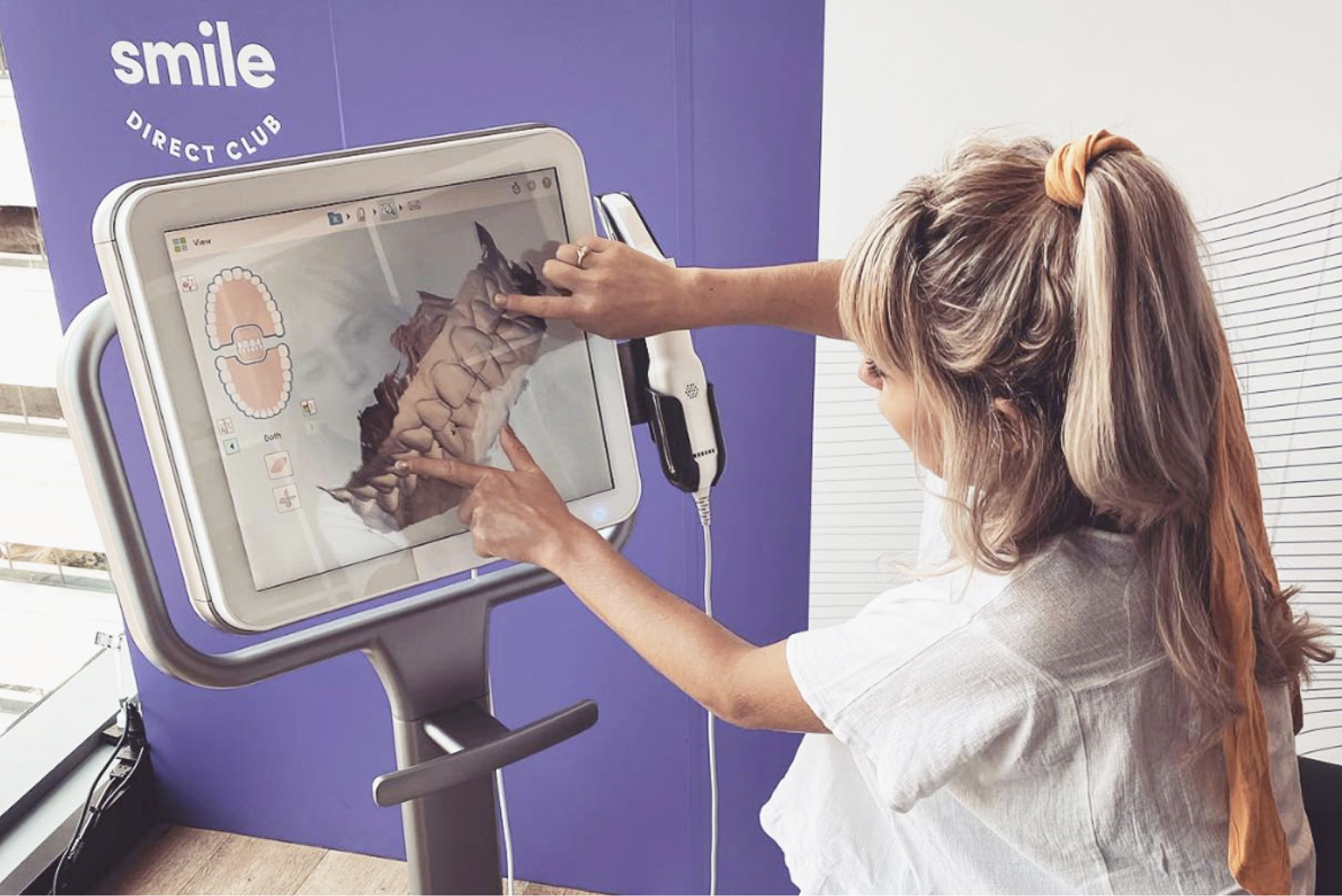 Blonde woman on white blouse and ponytail zooming her smile 3D scan at a Smileshop