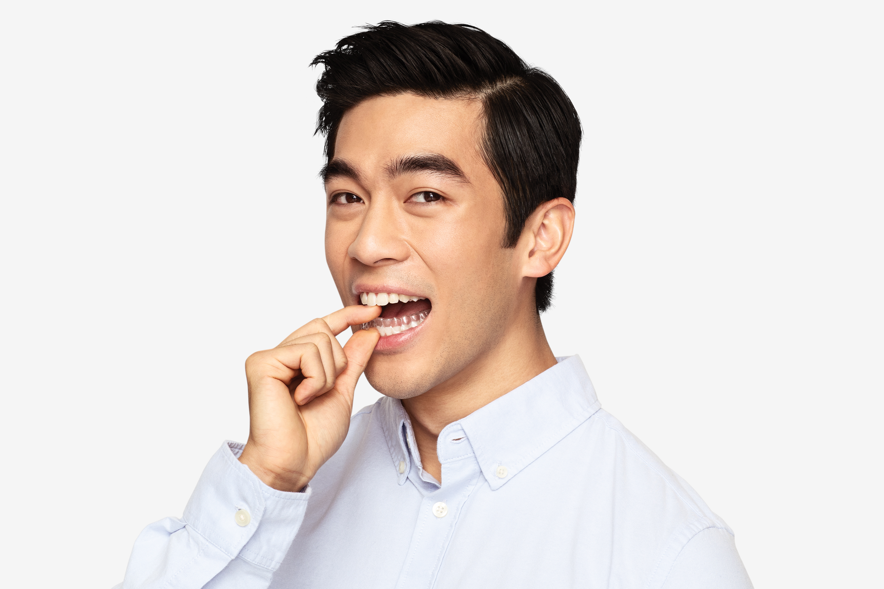 asian man wearing a blue collar button down shirt smiling and putting in smiledirectclub clear aligners