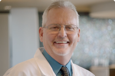 Smiling Dentist Dr. Gary Moore wearing white doctor coat and glasses headshot