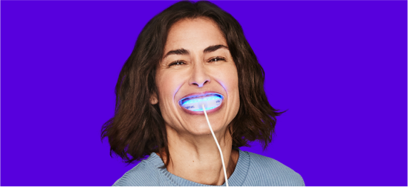 Woman smiling using a SmileDirectClub Teeth Whitening LED Light on blurple background