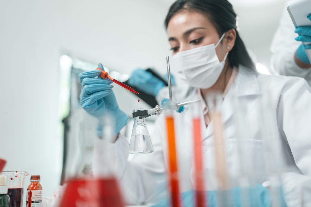Lab scientist using a pipette to drop liquid into a beaker