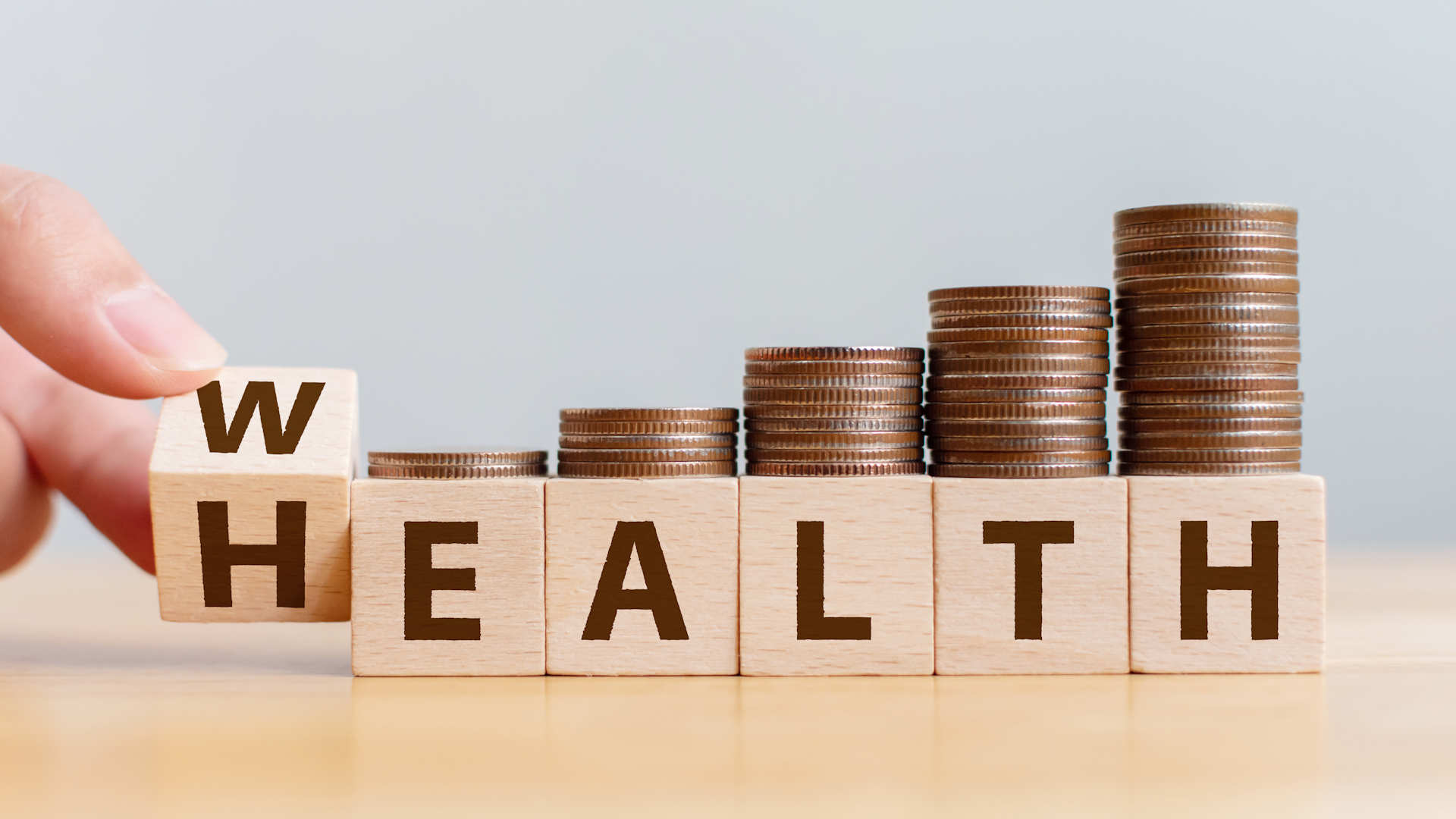Cubes in line, each having a lettes on it making words health with turning the first cube into wealth and money coins on top of each cube