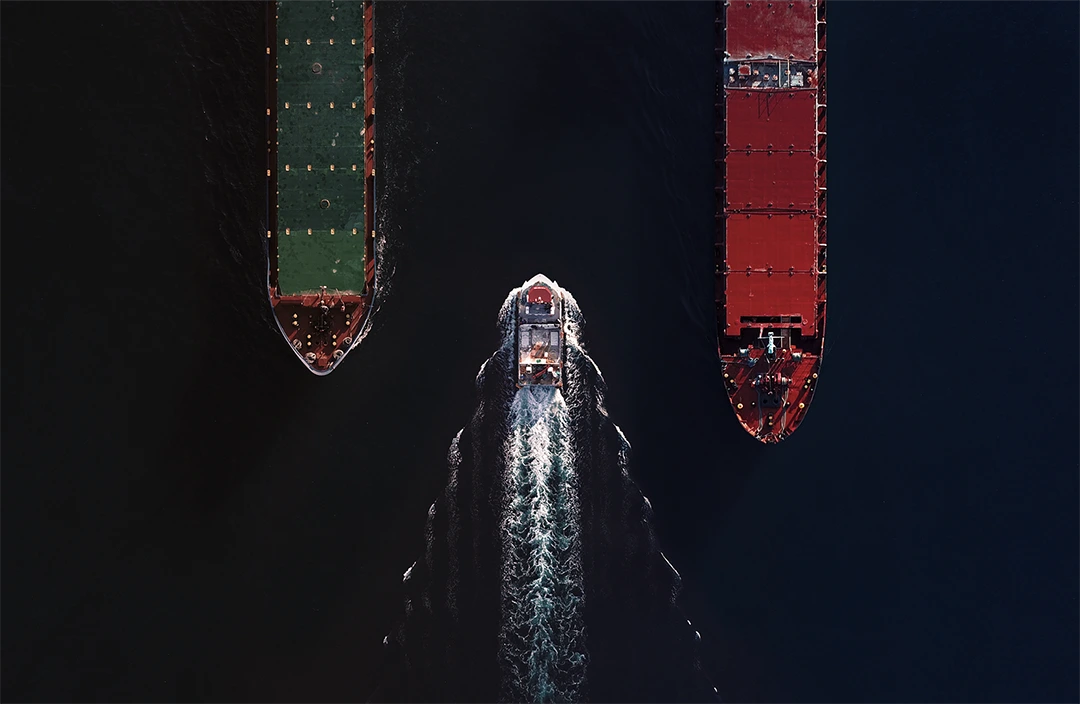Aerial view photo showing a small boat navigating between two large cargo ships in open water.