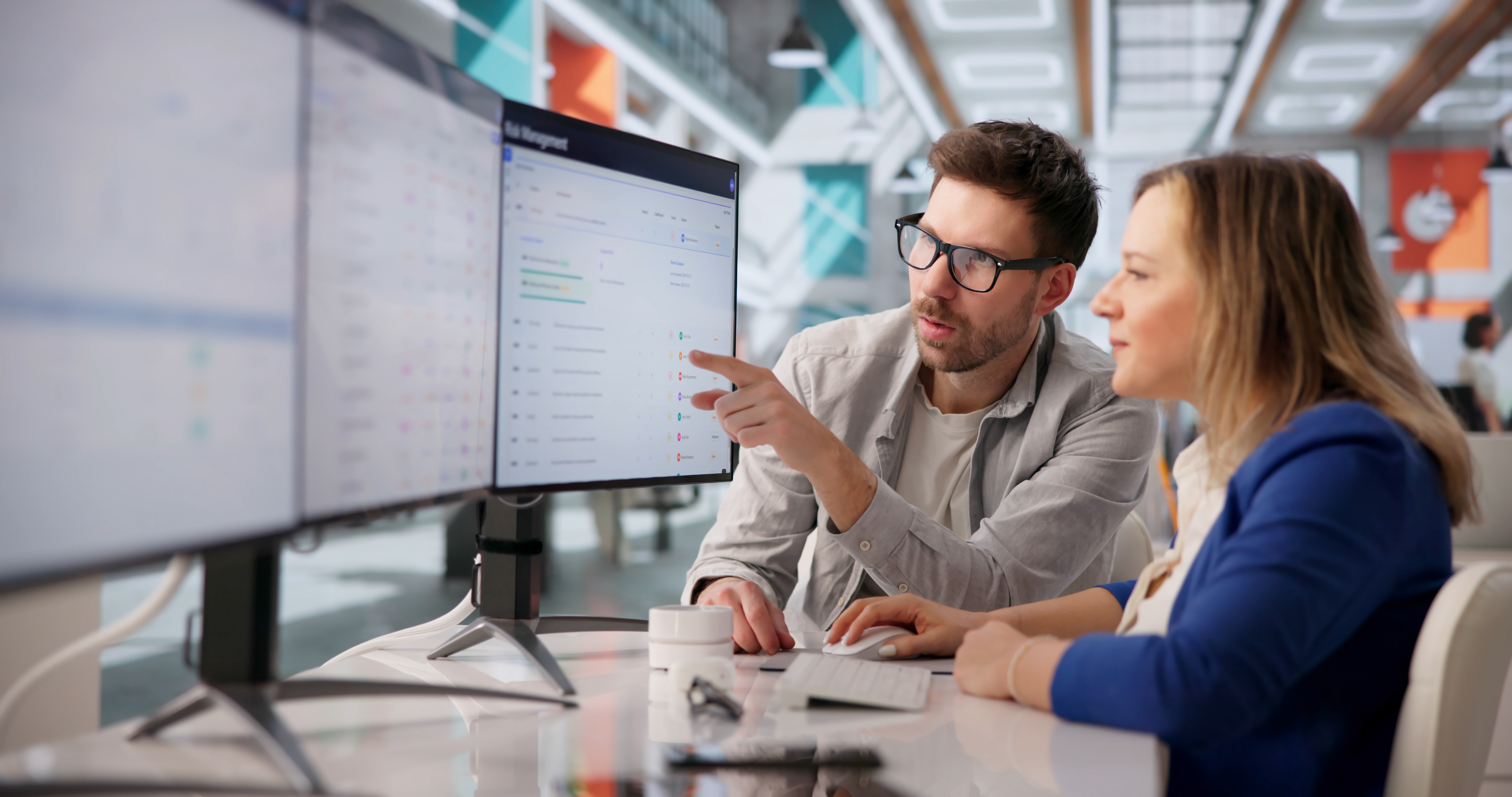 Two colleagues collaborate while looking at data on a computer screen.