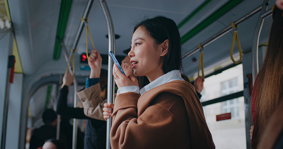 Image shows a passenger using a smartphone on a bus.