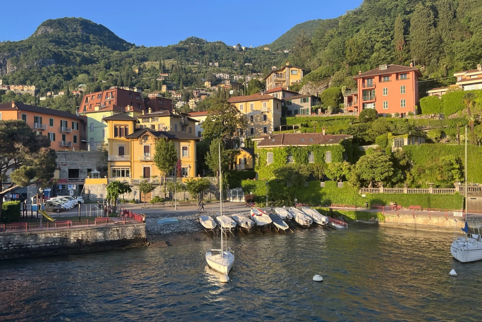 View of Villas in Lake Como and landscaped gardens by the lake and boats right before sunset.
