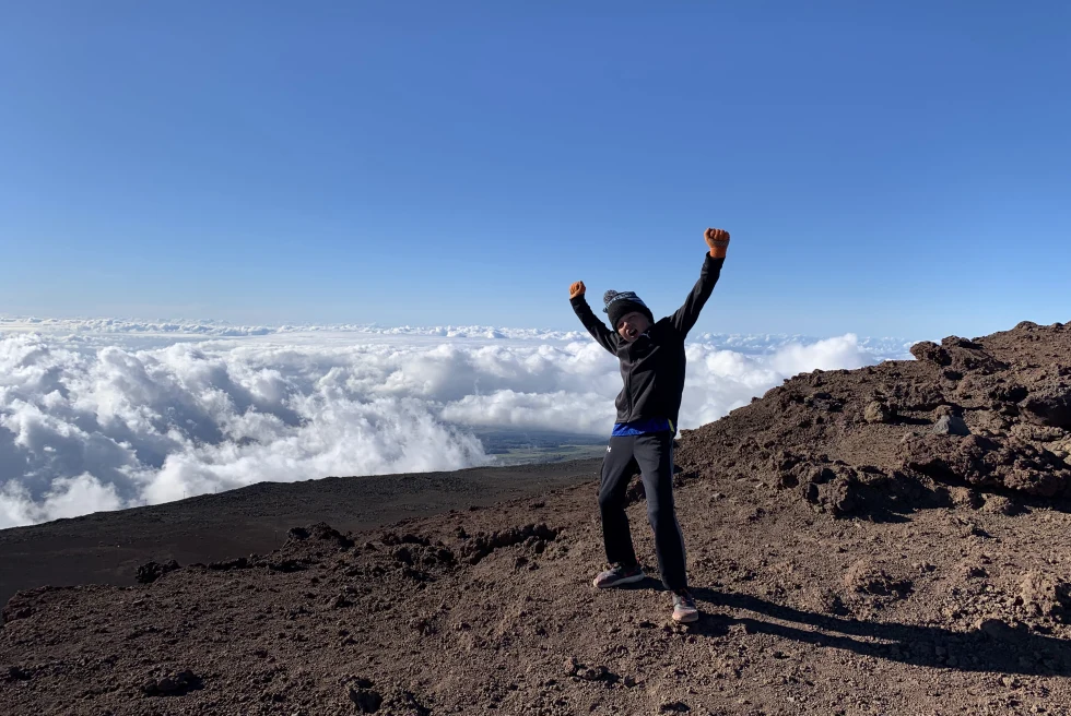 Boy standing on dark rock above the clouds during daytime