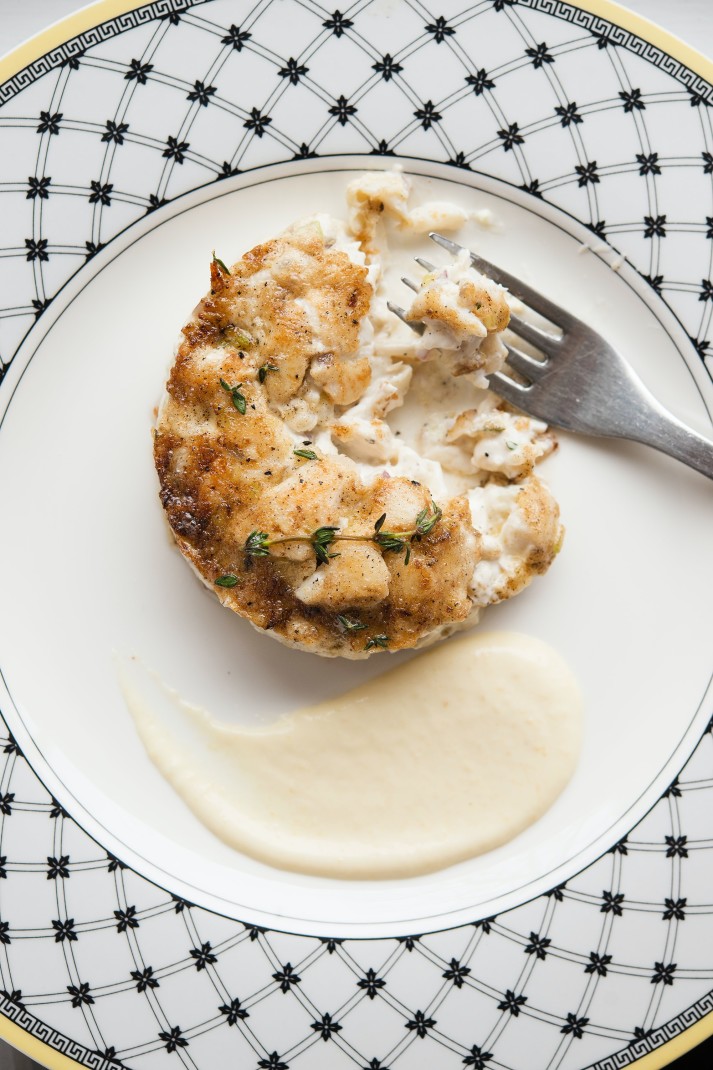 White plate with white sauce and crab cake with silver fork