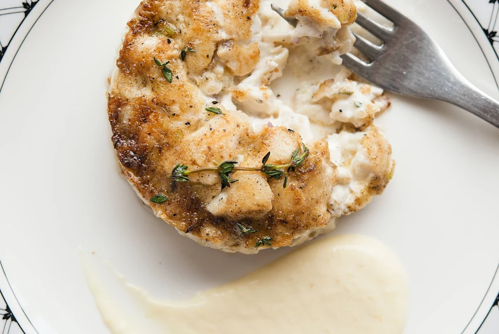 White plate with white sauce and crab cake with silver fork