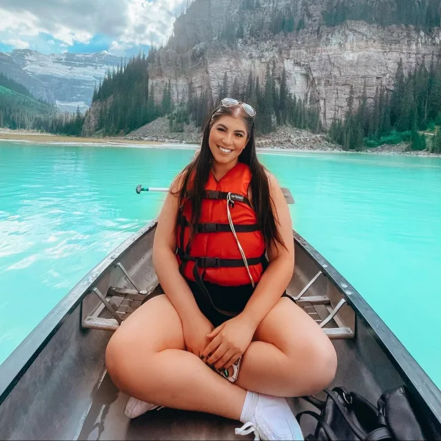 Picture of Alicia sitting on a canoe while wearing a red life vest over a ice blue lake. 