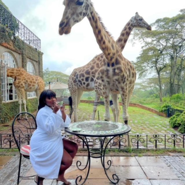 Fora travel agent Valerie Fervil sitting at table with giraffes in the background on a cloudy day