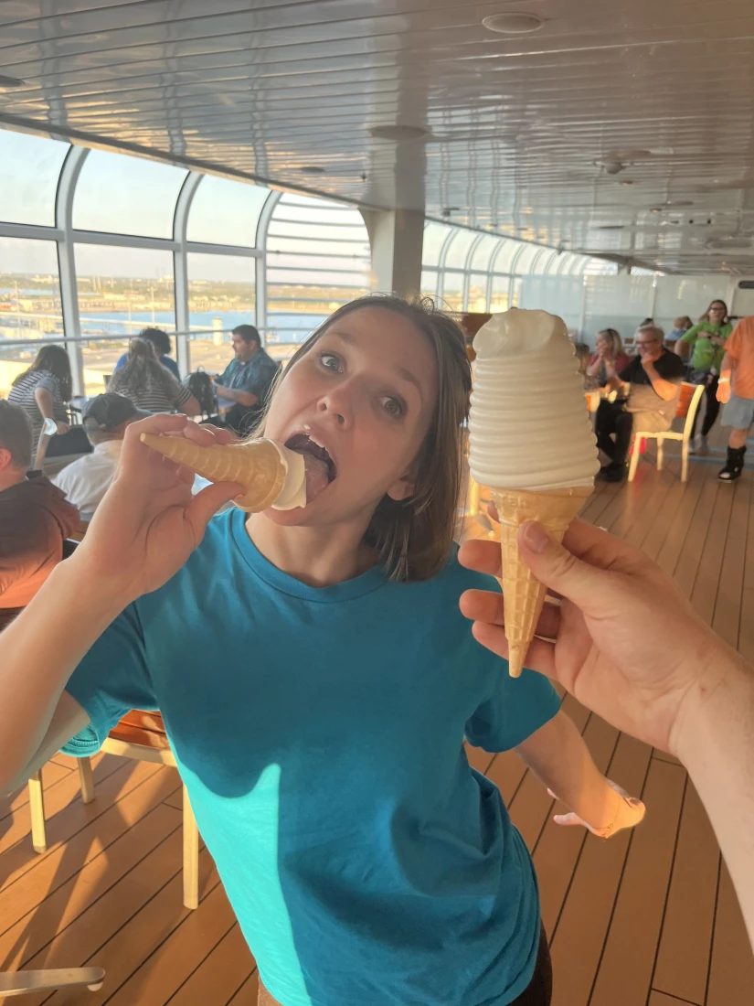 Travel advisor indulging in an ice cream cone, with someone holding another ice cream cone in front of her, with a view of the dining area in the background.