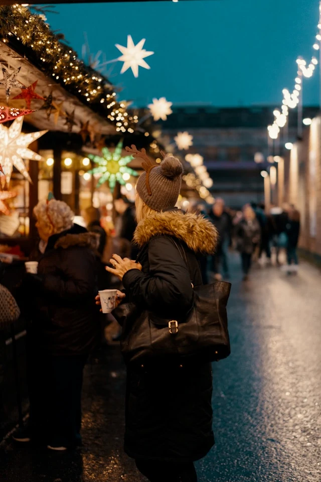 A view of people at the Chistmas Market in Ediburgh at night with christmas light decorations and market stands
