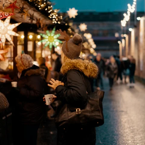 A view of people at the Chistmas Market in Ediburgh at night with christmas light decorations and market stands