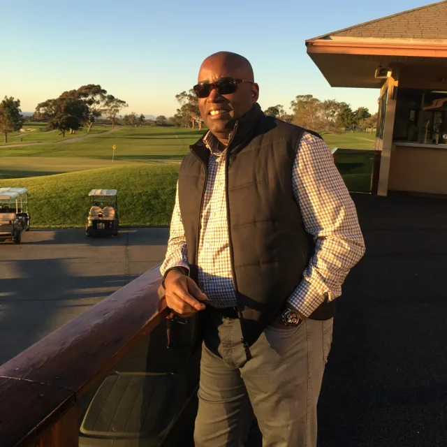 Travel Advisor Carl Johnson wearing sunglasses, a sleeveless jacket and standing in a golf course. 