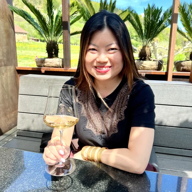 Travel advisor Anny Chen in a black shirt sits on a bench holding a wine glass