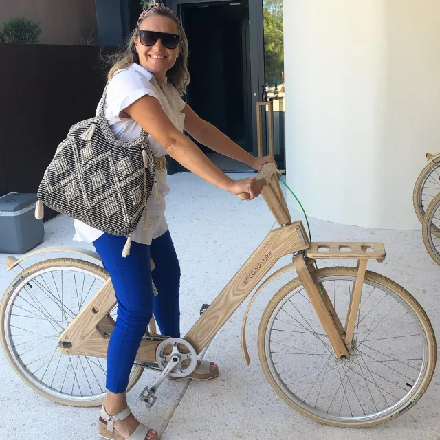 Nancy wearing a white top and blue pants on a wooden bicycle 