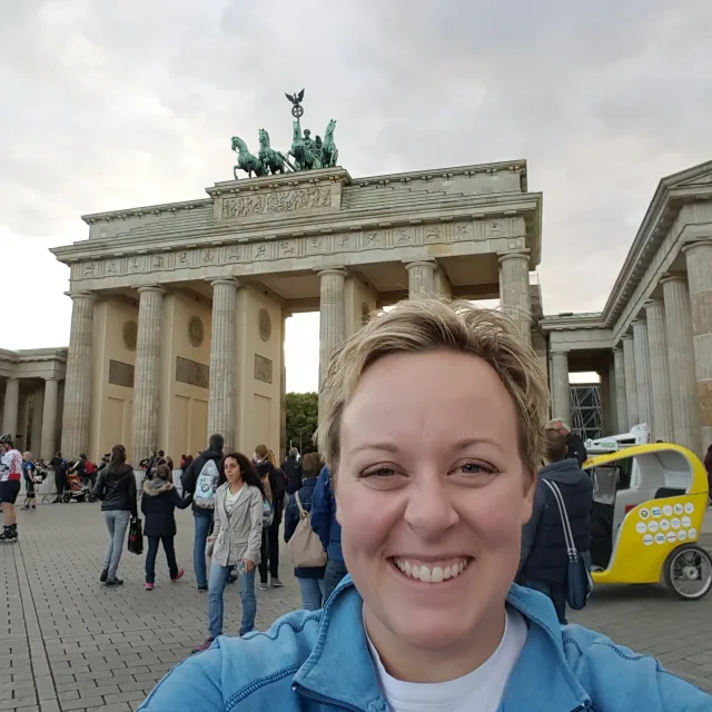 Travel Advisor Shannon Barnetts smiles for a selfie wearing a blue zip up and white t-shirt in front of a busy city monument.
