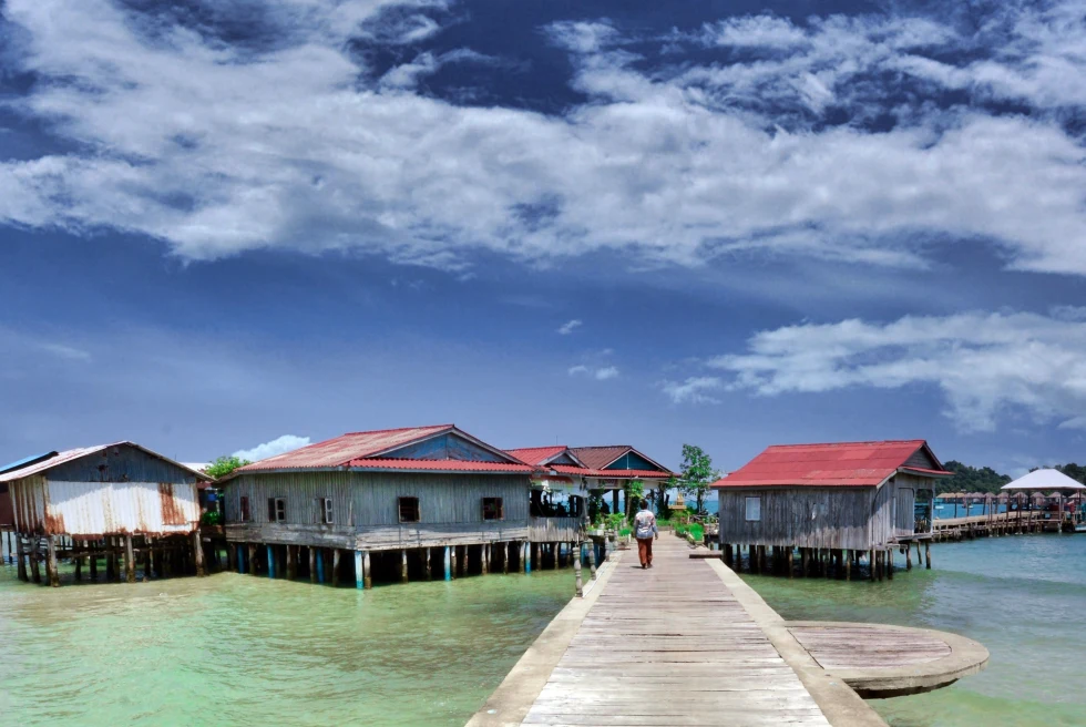 A resort with clear green water and pathway leading to huts. 