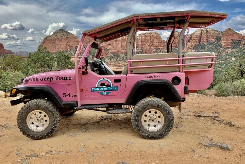Pink colored jeep in a dessert with mountains in background. 