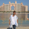 Fora travel agent Djoy Hassan wearing blue shirt and jeans standing in front of Atlantis in the Bahamas