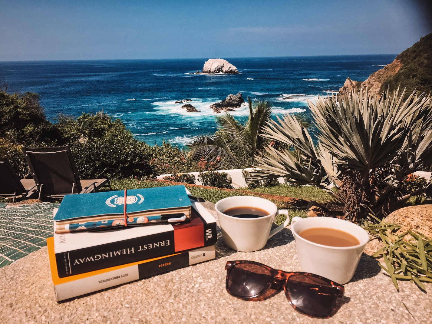 books and cups of coffee with the ocean in the background during daytime