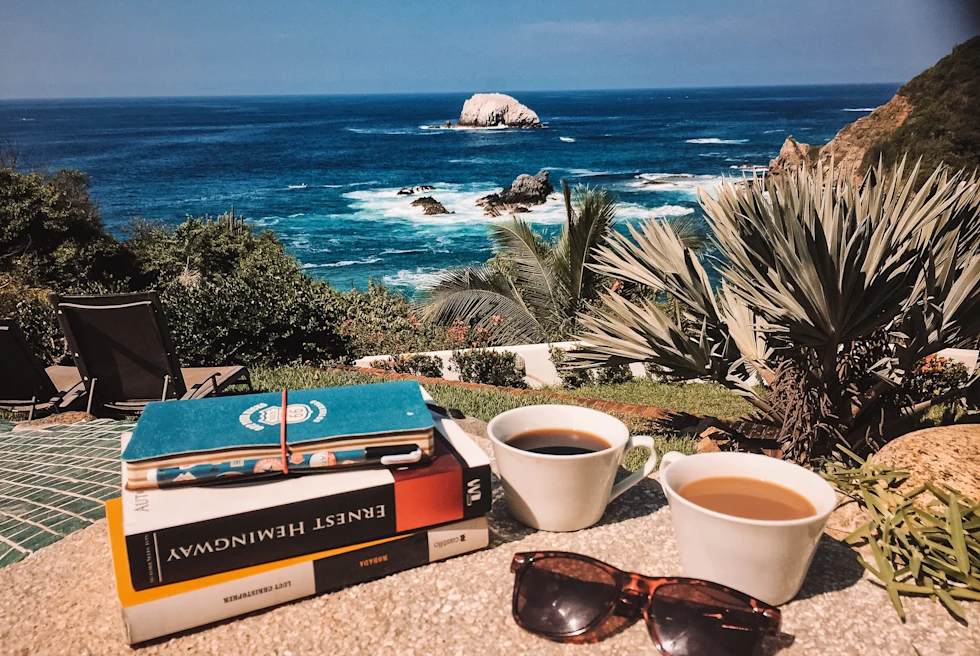 books and cups of coffee with the ocean in the background during daytime