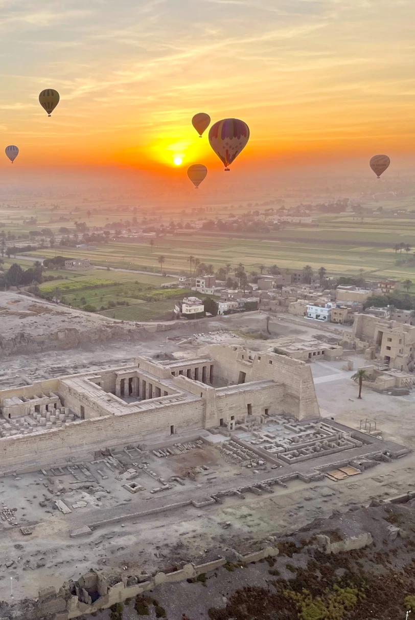 air balloons float in yellow sunrise over ancient desert ruins