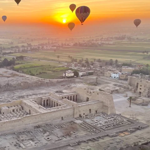 air balloons float in yellow sunrise over ancient desert ruins