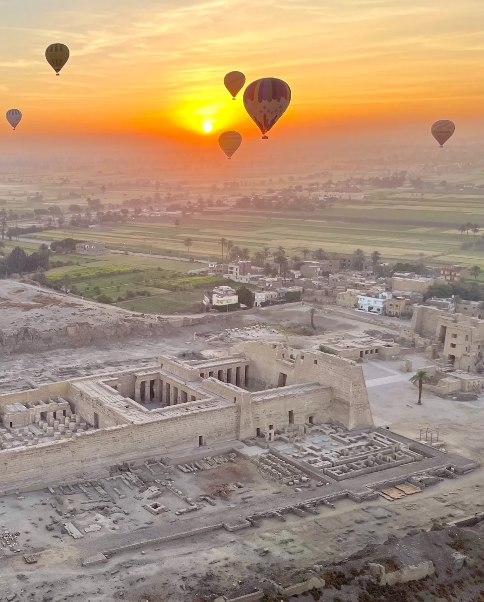 air balloons float in yellow sunrise over ancient desert ruins