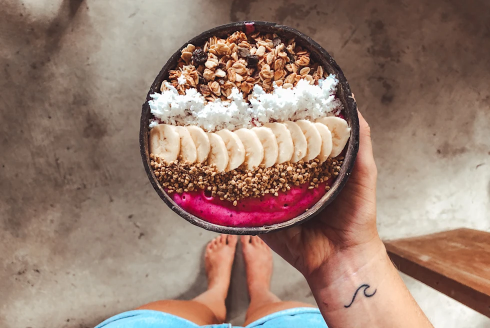 Smoothie bowl with pink, bananas and nuts help in one hand.