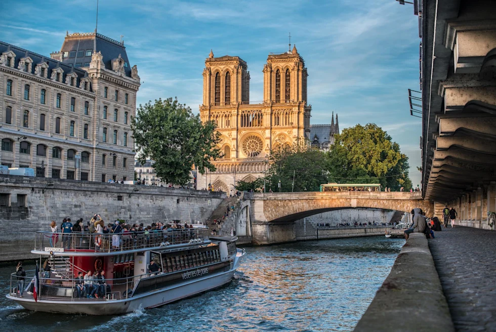 a boat cruises through a river in a city with the sun shining on a building ahead 