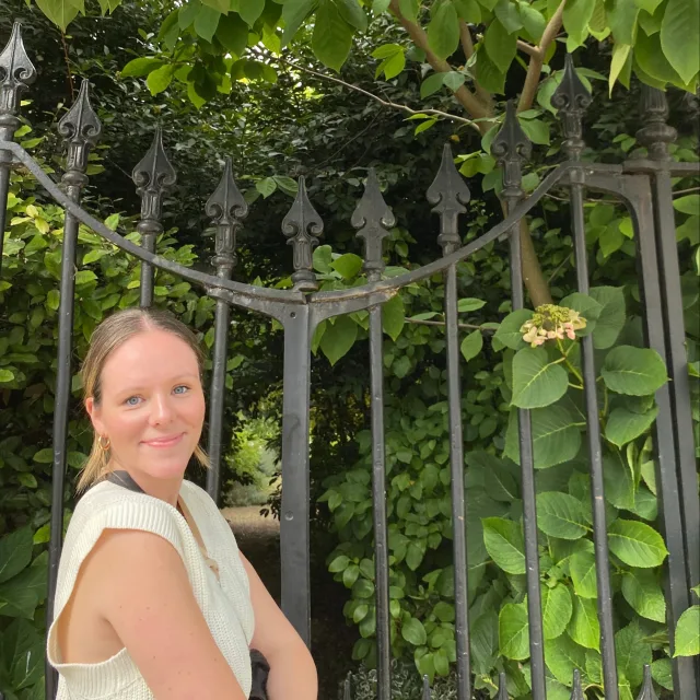 Travel Advisor Maggie Penn in a yellow shirt in front of green plants and an iron gate.