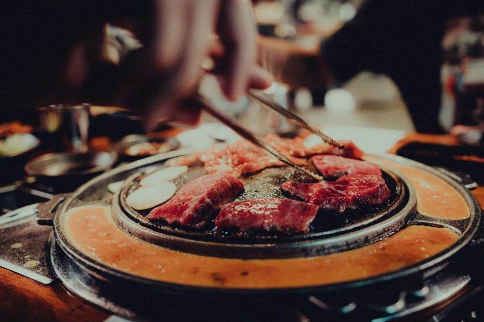 person holding chopsticks over steak on a grill