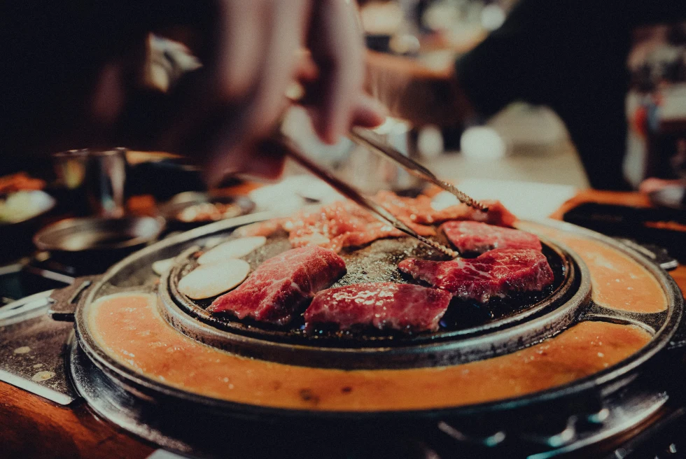person holding chopsticks over steak on a grill