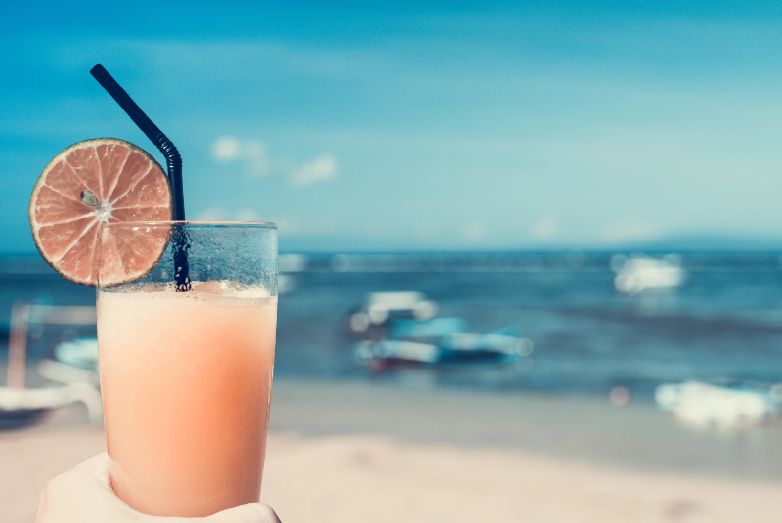 Pink drink in a glass with a black straw with beach in the background