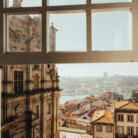 Window view of Porto featuring a street, church, ocean and local houses. 
