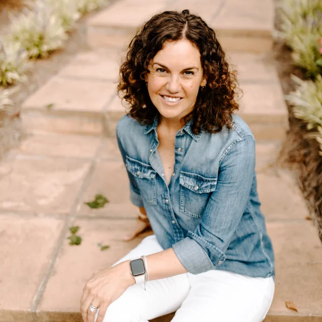 Travel Advisor Juli Hall sitting outdoors on stairs in denim shirt.