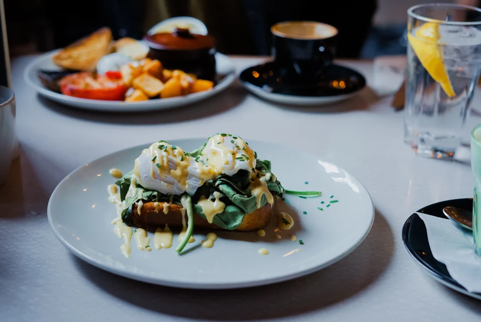 brunch in philadelphia eggs on toast and lettuce hollandaise on white plate with coffee water with lemon and ice in clear glass